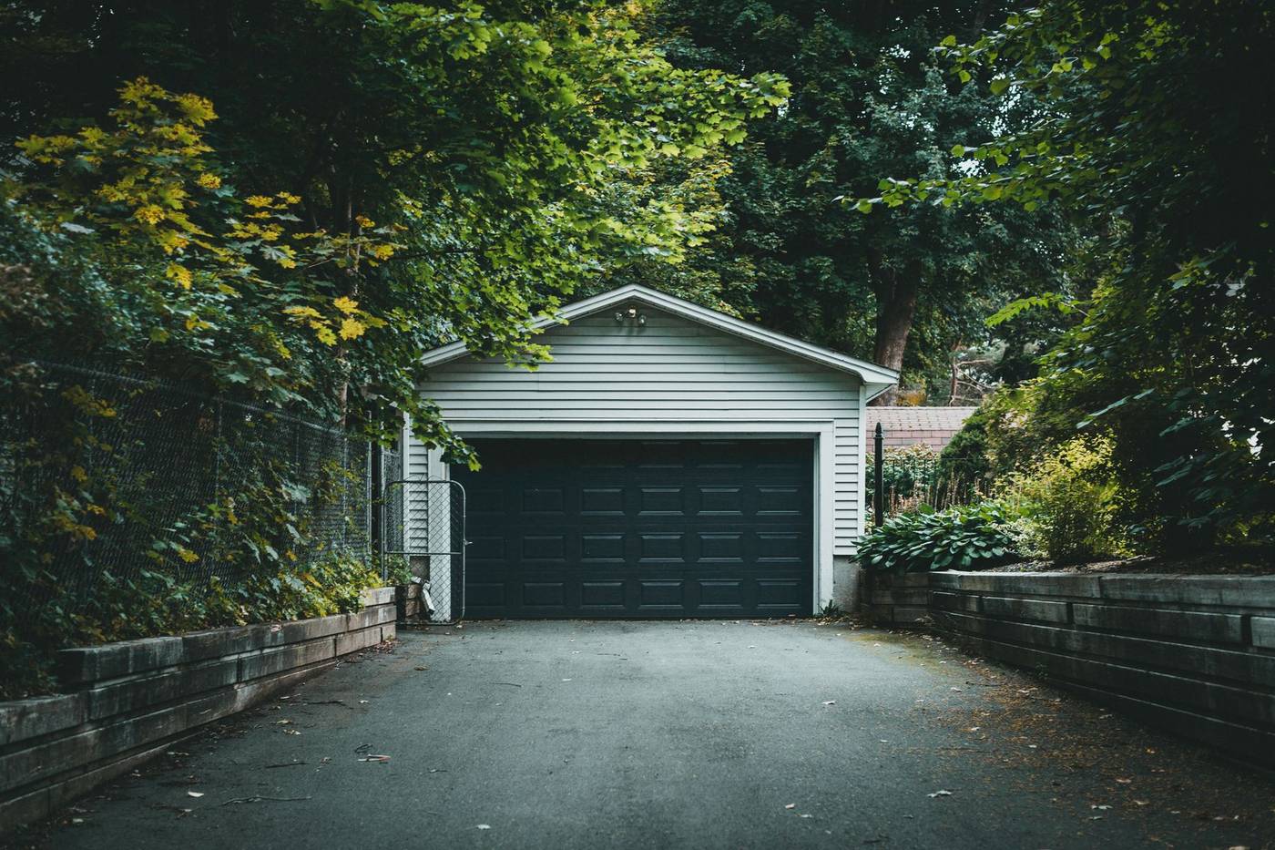 Dark asphalt driveway leading to a white garage, framed by green trees